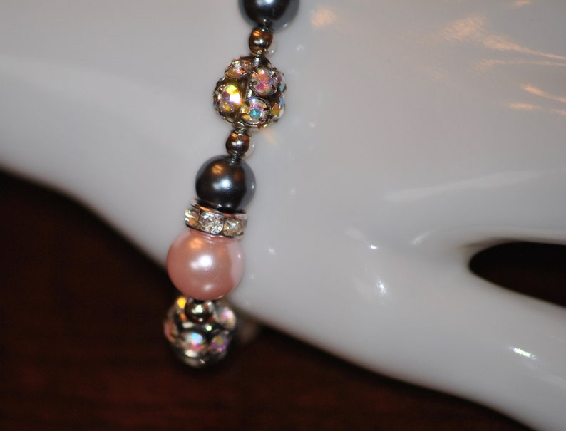 May include: A bracelet with pink, gray, and clear beads. The beads are interspersed with silver spacers. The bracelet is on a white mannequin hand.
