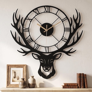 May include: A black metal wall clock featuring a stylized deer head silhouette with large antlers framing a circular clock face. The clock face displays Roman numerals and thin gold-colored hands, mounted centrally above a fireplace mantel.