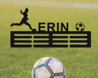 May include: Black metal soccer medal holder with the name "ERIN" and a silhouette of a soccer player kicking a ball. The holder has 8 slots for medals.