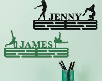 May include: Two personalized medal hangers, one green and one black, with gymnast silhouettes and names "JAMES" and "JENNY".