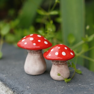 Op de afbeelding: Twee keramische paddenstoelen met rode en witte stippen op de hoeden en bruine stelen. De paddenstoelen zijn verschillend van grootte.