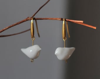 Puede incluir: Un par de pendientes de aro de oro con colgantes de pájaro de porcelana blanca.