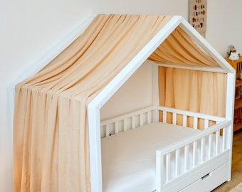 May include: A white wooden house-shaped bed frame with a peach-colored canopy and matching curtains. The bed has a white mattress and two drawers. A garland of triangular flags hangs above the bed.