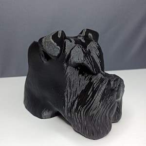 May include: A black 3D printed sculpture of a miniature schnauzer dog's head. The sculpture is detailed with fur and facial features.