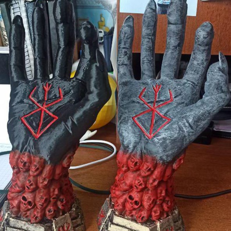Puede incluir: Dos manos impresas en 3D de color negro y gris con un s&iacute;mbolo rojo en la palma. Las manos est&aacute;n cubiertas de cr&aacute;neos rojos. Las manos est&aacute;n sobre una base de madera.
