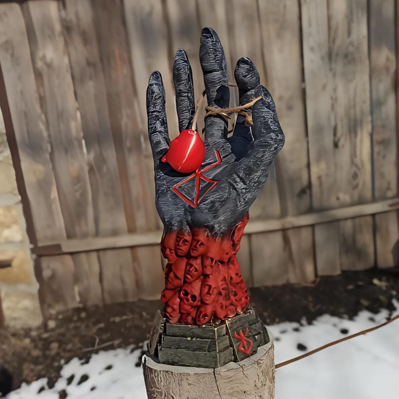 Puede incluir: Una mano negra con un s&iacute;mbolo rojo y un dije de coraz&oacute;n rojo colgando de ella. La mano est&aacute; cubierta de peque&ntilde;as caras rojas. La mano est&aacute; sobre una base de madera.