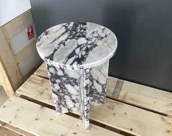 May include: A round marble side table with a white and purple marbled top and a base with four legs. The table is sitting on a wooden pallet.