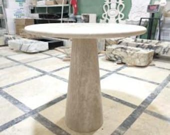May include: A round, white marble table with a pedestal base. The table top is smooth and the base is textured.