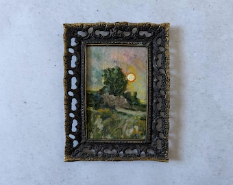 May include: An antique landscape oil painting in a decorative, ornate frame. The artwork depicts a tree, a setting sun, and a grassy field. The frame is dark with gold accents.