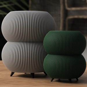 Könnte beinhalten: Zwei dekorative Keramik-Blumentöpfe mit geripptem Design. Der größere Topf ist grau und der kleinere ist grün.