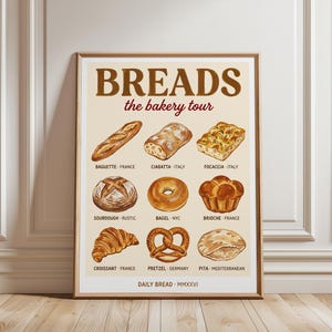 Peut inclure: Une affiche encadrée intitulée BREADS the bakery tour, illustrant neuf variétés de pains dont baguette, ciabatta, focaccia, sourdough, bagel, brioche, croissant, pretzel et pita, avec leurs origines et le texte DAILY BREAD MMXXVI en bas.