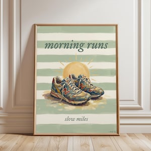 Op de afbeelding: Een ingelijste kunstdruk met een paar sportschoenen op een gestructureerde ondergrond. De achtergrond heeft horizontale saliegroene en crèmekleurige strepen, een gele zon en de tekst "morning runs" bovenaan en "slow miles" onderaan.