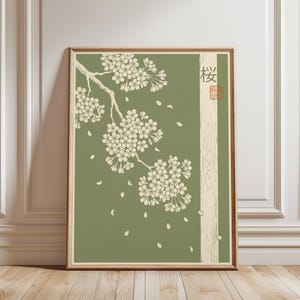 Op de afbeelding: Een ingelijste kunstdruk met een tak met kersenbloesems tegen een gedempte groene achtergrond. De Japanse karakters voor "kers" staan rechts op de print.