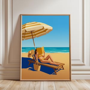 May include: A framed art print depicting a person in a yellow bikini lounging on a wooden beach chair under a yellow and white striped umbrella. The person is reading a yellow book on a sandy beach with a straw hat and a woven tote bag nearby.