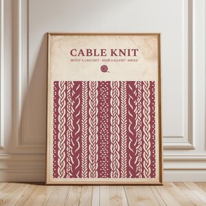 May include: A framed vertical wall art print featuring a cream-colored background with the text CABLE KNIT, MOTIF A CROCHET, NOIR GALLERY, MMXII and a small yarn ball icon. Below, a deep red section displays a repeating vertical cable knit pattern.