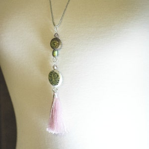 May include: A silver chain necklace with a pink tassel, a green and white patterned bead, and a green and gold bead.