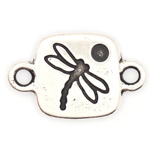 May include: Silver-toned metal charm with a dragonfly design and a small circle. The charm has two loops for attaching to a bracelet or necklace.