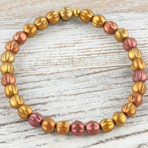 May include: A gold and rose gold beaded bracelet with a textured finish. The beads are round and have a slightly raised design.