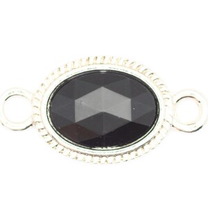 May include: A silver oval connector with a black faceted gemstone. The connector has two loops on either side for attaching jewelry.
