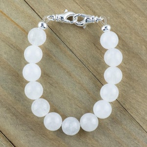 May include: A white gemstone bracelet with a silver clasp. The bracelet is made of round, smooth beads.