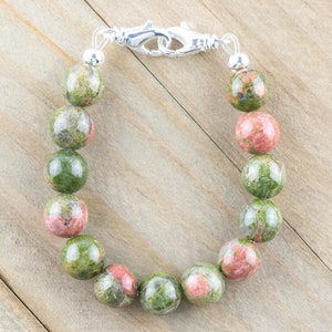 Puede incluir: Un brazalete de piedras preciosas verdes, rosas y blancas con un cierre plateado.