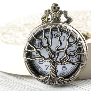May include: A bronze pocket watch featuring a tree of life design. The watch face is white with black numerals and hands. The watch is set on a white surface. The watch's diameter is approximately 4 cm.