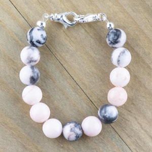 May include: A pink and black gemstone bracelet with a silver clasp. The bracelet is made of round beads and is approximately 18 cm long.