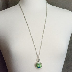 May include: A silver chain necklace with a round pendant featuring a peacock design in green and blue colours.