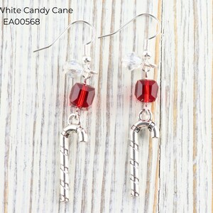 Pode incluir: Um par de brincos com tema natalino. Cada brinco apresenta uma conta vermelha facetada, um pingente de bengala doce prateado e um detalhe de cristal transparente. O texto "Red & White Candy Cane EA00568" &eacute; vis&iacute;vel.