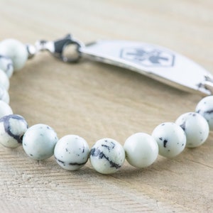Peut inclure: Un bracelet en perles de pierre blanches et noires avec une plaque d'identification m&eacute;dicale en argent. La plaque comporte un symbole m&eacute;dical et un espace pour la gravure.