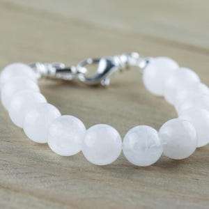 May include: A white gemstone bracelet with a silver clasp. The bracelet is made of round, smooth beads.