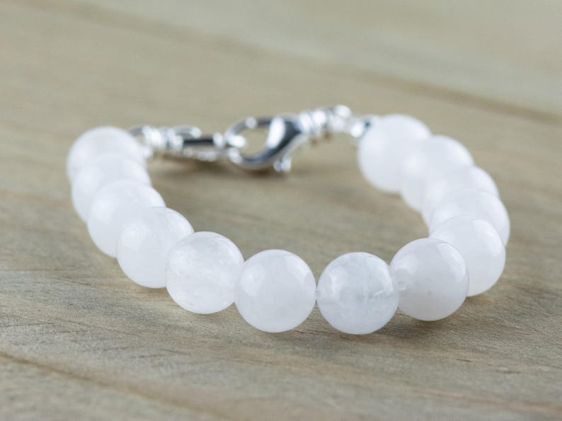 May include: A white gemstone bracelet with a silver clasp. The bracelet is made of round, smooth beads.