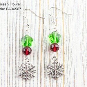 Pode incluir: Brincos pendurados com um design festivo. Cada brinco apresenta uma conta verde em forma de flor, uma conta redonda vermelha e um pingente de floco de neve prateado. O texto "Red & Green Flower Snowflake EA00567" &eacute; vis&iacute;vel.