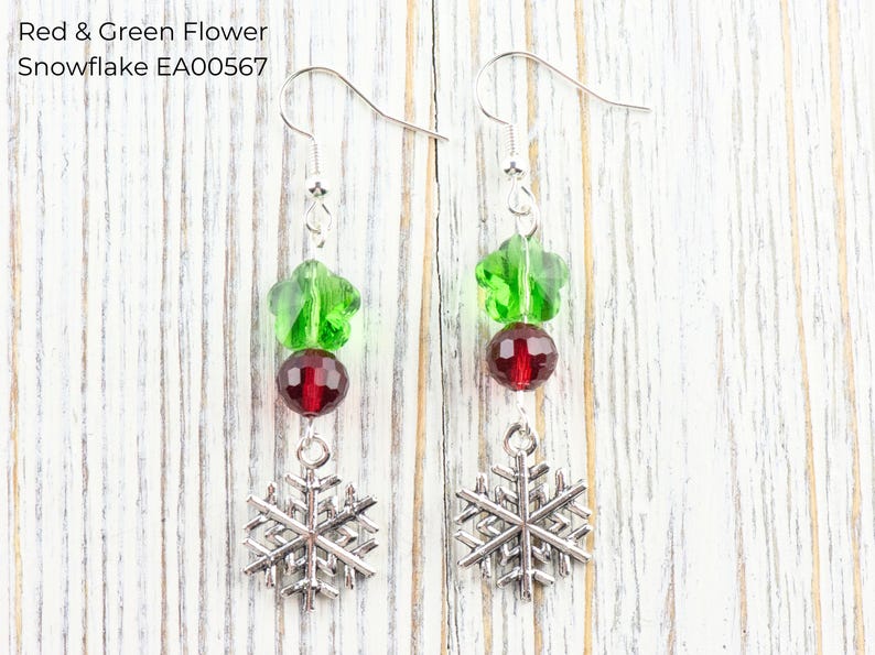 Pode incluir: Brincos pendurados com um design festivo. Cada brinco apresenta uma conta verde em forma de flor, uma conta redonda vermelha e um pingente de floco de neve prateado. O texto "Red & Green Flower Snowflake EA00567" &eacute; vis&iacute;vel.