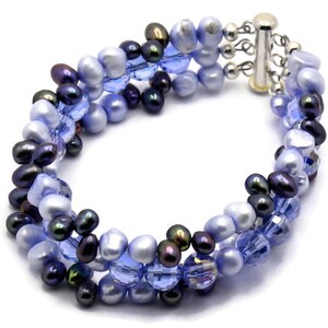 May include: A multi-strand bracelet featuring a mix of blue and black beads. The bracelet is made with small, round, iridescent blue beads, dark blue beads, and black beads. The bracelet has a silver clasp.