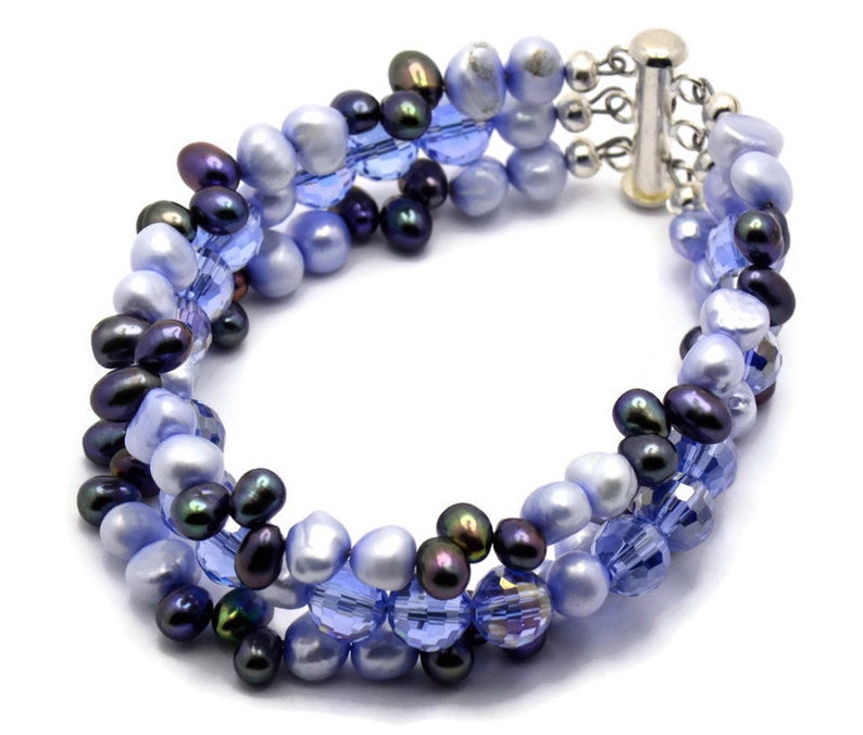 May include: A multi-strand bracelet featuring a mix of blue and black beads. The bracelet is made with small, round, iridescent blue beads, dark blue beads, and black beads. The bracelet has a silver clasp.
