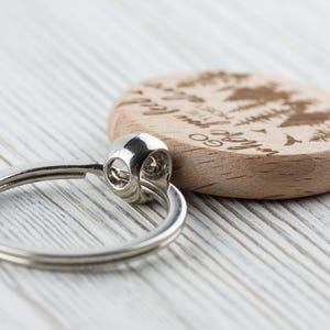 May include: A wooden keychain with a silver ring. The wood is light brown and has a design of trees and the text "Go where you feel most alive".