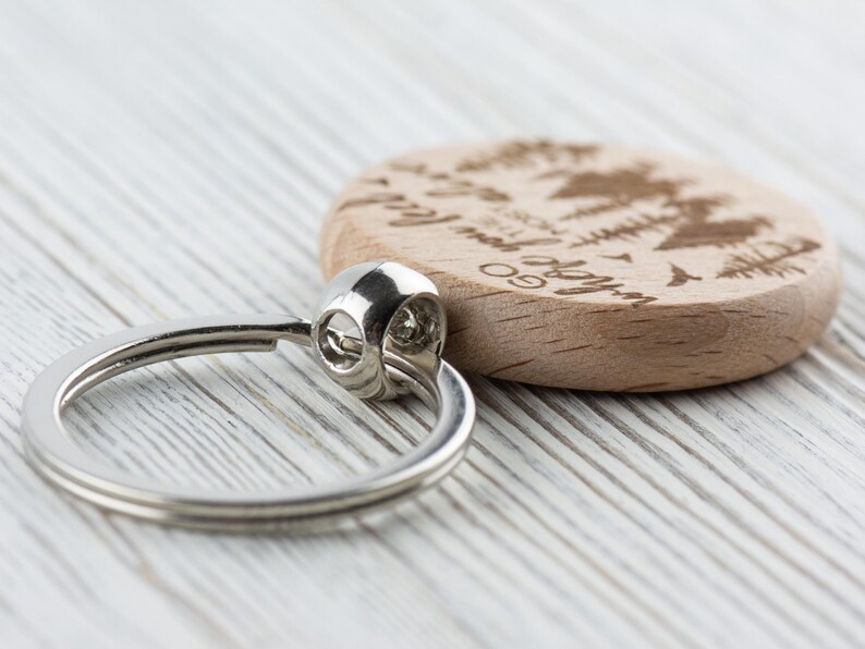 May include: A wooden keychain with a silver ring. The wood is light brown and has a design of trees and the text "Go where you feel most alive".