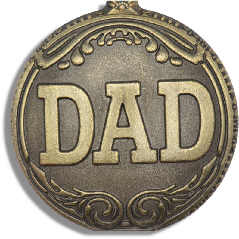 Peut inclure: Une d&eacute;coration ronde en m&eacute;tal dor&eacute; avec un motif orn&eacute; et le mot "DAD" en relief au centre.