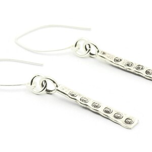 May include: A pair of silver dangle earrings with a textured bar design. Each bar has a series of small circles embossed on the surface.