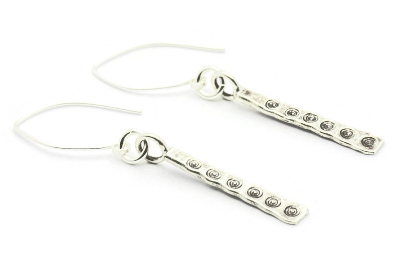 May include: A pair of silver dangle earrings with a textured bar design. Each bar has a series of small circles embossed on the surface.