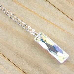 Pu&ograve; includere: Una collana con catena d'argento con un ciondolo di cristallo trasparente. Il ciondolo &egrave; rettangolare e ha un design sfaccettato.