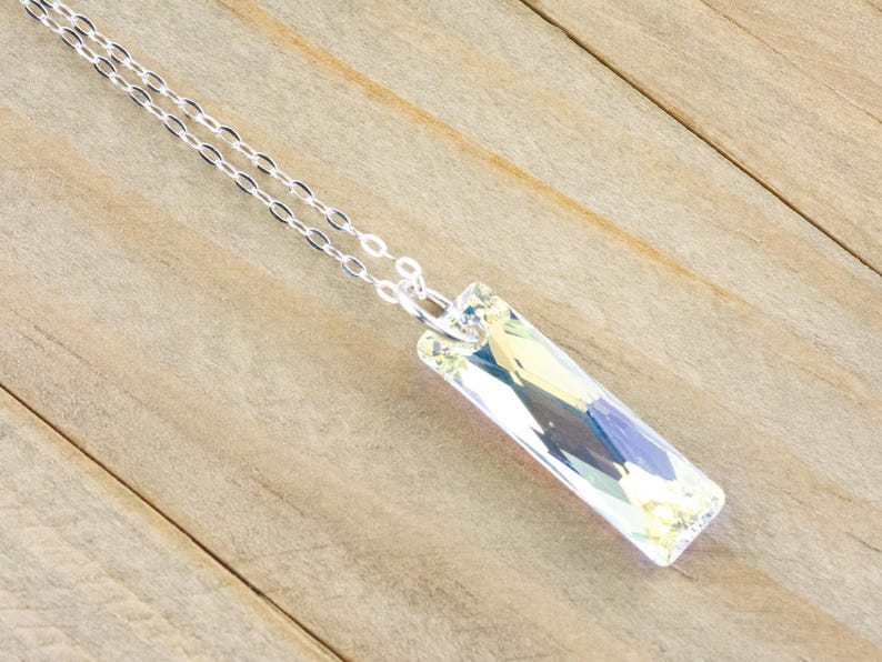 Pu&ograve; includere: Una collana con catena d'argento con un ciondolo di cristallo trasparente. Il ciondolo &egrave; rettangolare e ha un design sfaccettato.