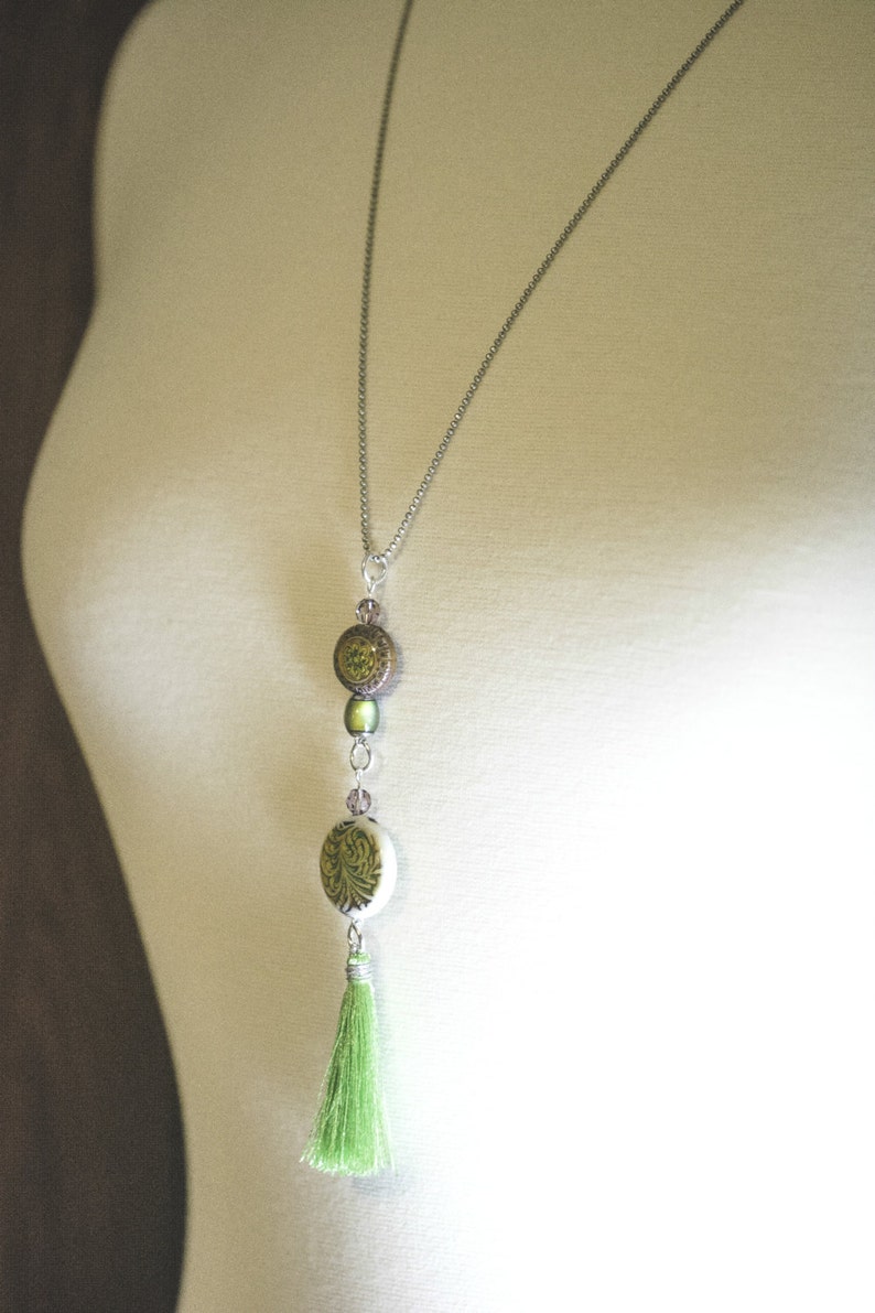 May include: A silver chain necklace with a green tassel and three round green and brown beads.