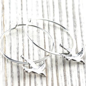 Peut inclure: Boucles d'oreilles cr&eacute;oles argent&eacute;es avec un charm en forme d'oiseau. Les boucles d'oreilles pr&eacute;sentent un design circulaire simple avec un petit pendentif oiseau d&eacute;taill&eacute;. Les oiseaux sont en vol, ajoutant une touche d'&eacute;l&eacute;gance inspir&eacute;e de la nature.