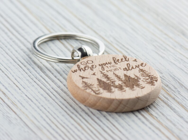 May include: Wooden keychain with a silver key ring. The keychain is engraved with the text "Go where you feel the most alive" and a silhouette of trees.