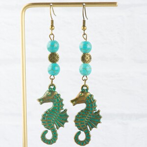 May include: A pair of turquoise and bronze seahorse earrings. Each earring features three turquoise beads and a bronze charm, with a seahorse pendant at the bottom.