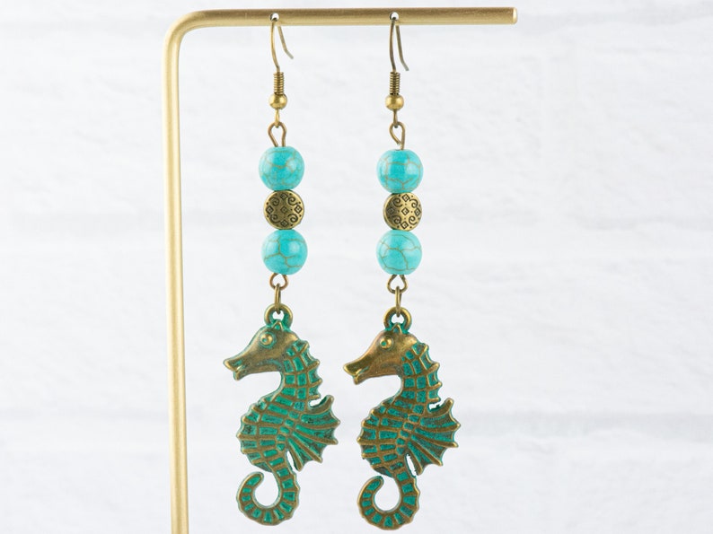 May include: A pair of turquoise and bronze seahorse earrings. Each earring features three turquoise beads and a bronze charm, with a seahorse pendant at the bottom.