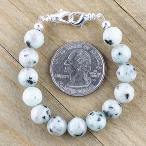 K&ouml;nnte beinhalten: Ein wei&szlig;es und schwarz geflecktes Stein-Armband mit einem silbernen Verschluss. Das Armband ist etwa so gro&szlig; wie eine 25-Cent-M&uuml;nze.
