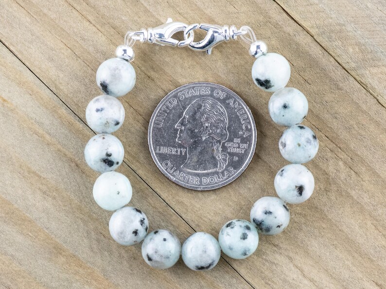K&ouml;nnte beinhalten: Ein wei&szlig;es und schwarz geflecktes Stein-Armband mit einem silbernen Verschluss. Das Armband ist etwa so gro&szlig; wie eine 25-Cent-M&uuml;nze.